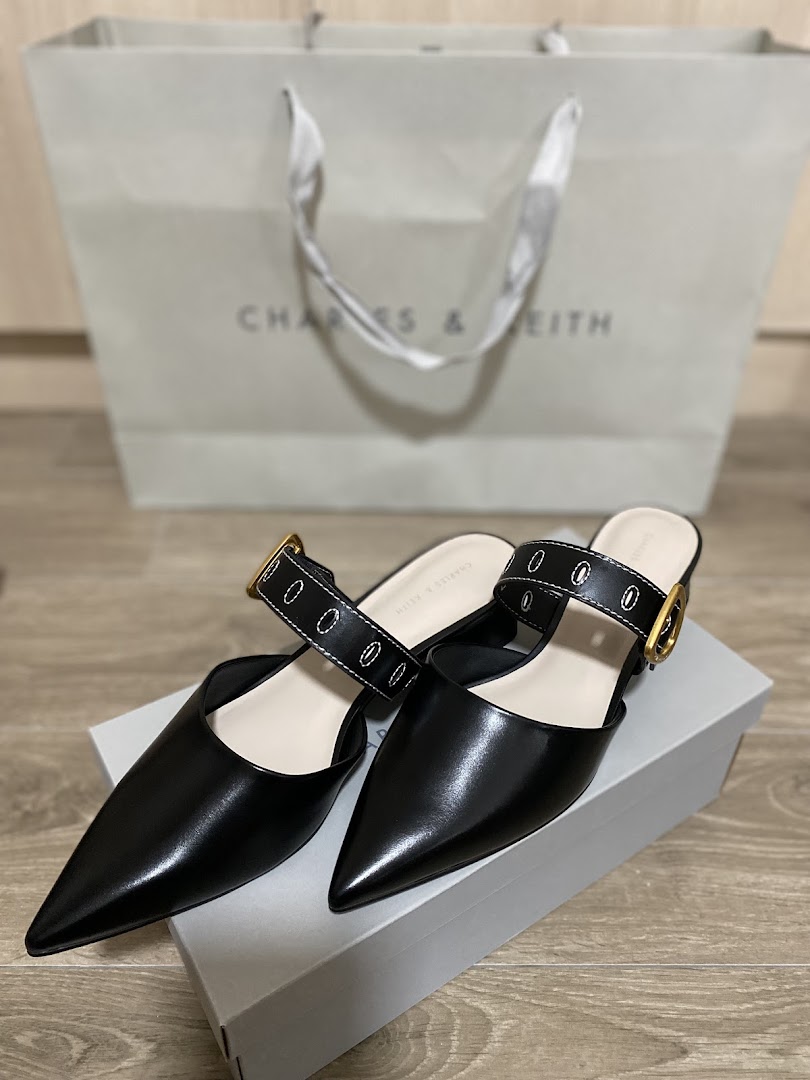 Stylish black pointed-toe mules with a buckle strap, displayed with a CHARLES & KEITH shopping bag.