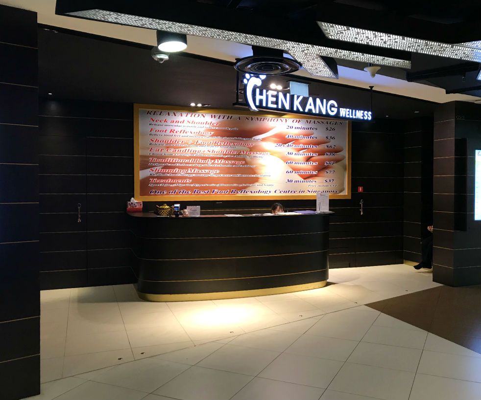 Reception area of Chen Kang Wellness featuring a large sign with massage and reflexology services and prices.