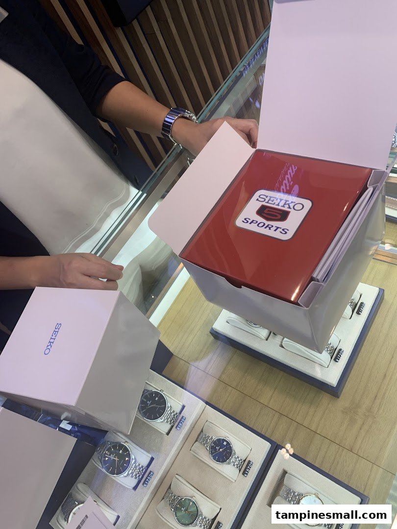 A customer opens a Seiko watch box at a display counter in City Chain, surrounded by various watches.