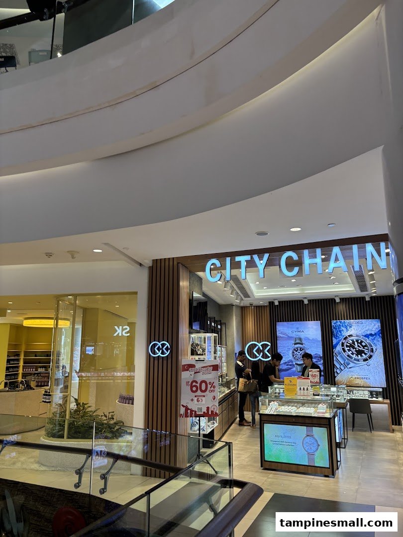 The City Chain shop entrance in a mall, featuring illuminated signage, watch displays, and customers.