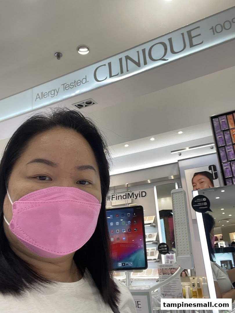 A person in a pink mask inside a Clinique store, with the brand's 'Allergy Tested' signage visible.