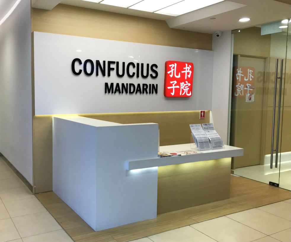 The bright, modern reception area of Confucius Mandarin, featuring a prominent logo and information desk.