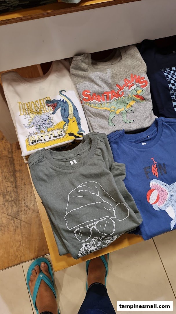 A top-down view of colorful, folded children's graphic t-shirts displayed in a retail store.
