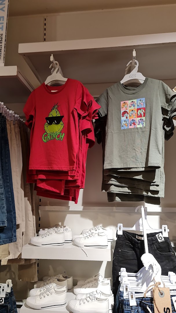 A retail display featuring children's graphic t-shirts (Grinch, pop art) and white sneakers on shelves.