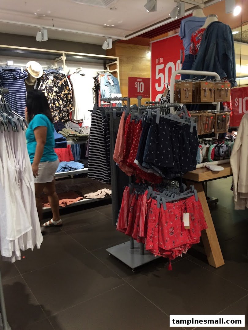 Interior view of Cotton On Tampines, showcasing clothing racks, sale items, and a shopper browsing.
