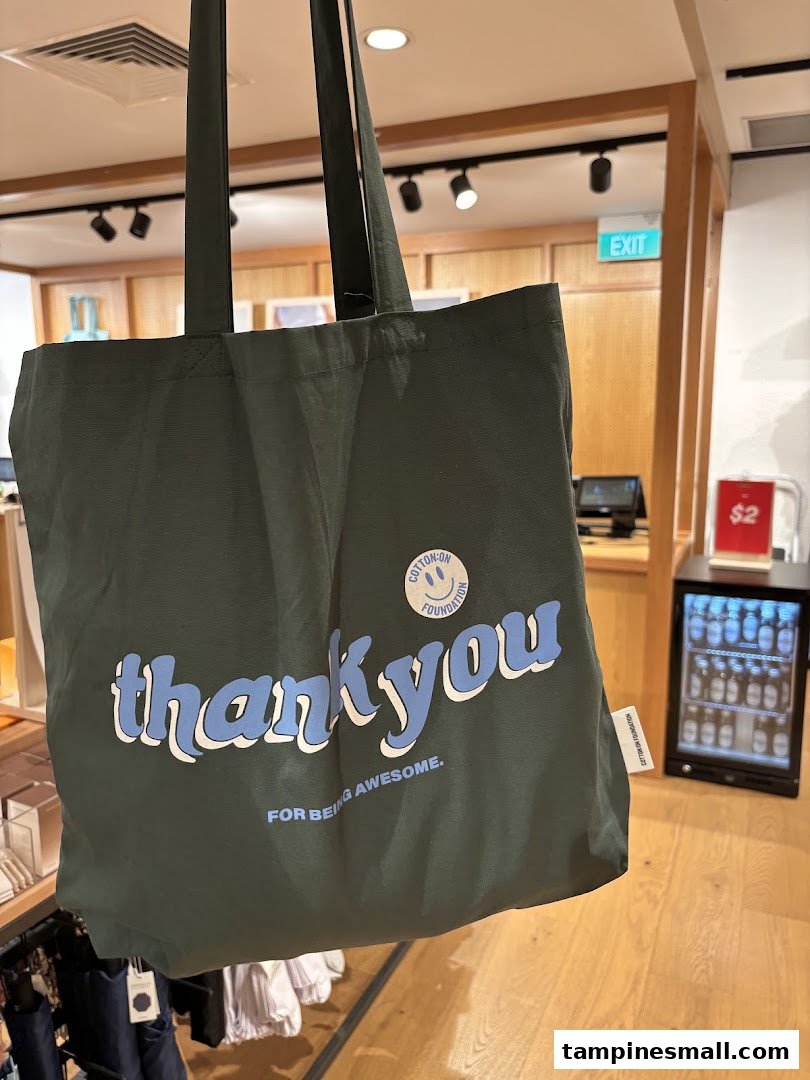 A dark green Cotton On Foundation tote bag with 'thank you' text, displayed inside the store.