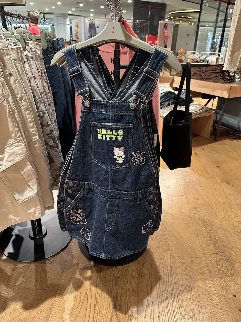 A denim overall dress with Hello Kitty and floral embroidery displayed in a retail store.