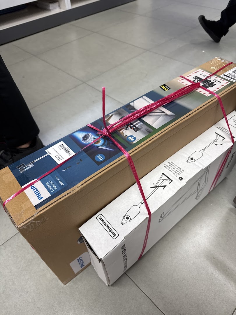 Two boxed Philips products, a cordless vacuum and a stand, tied together with pink string, on a tiled floor.