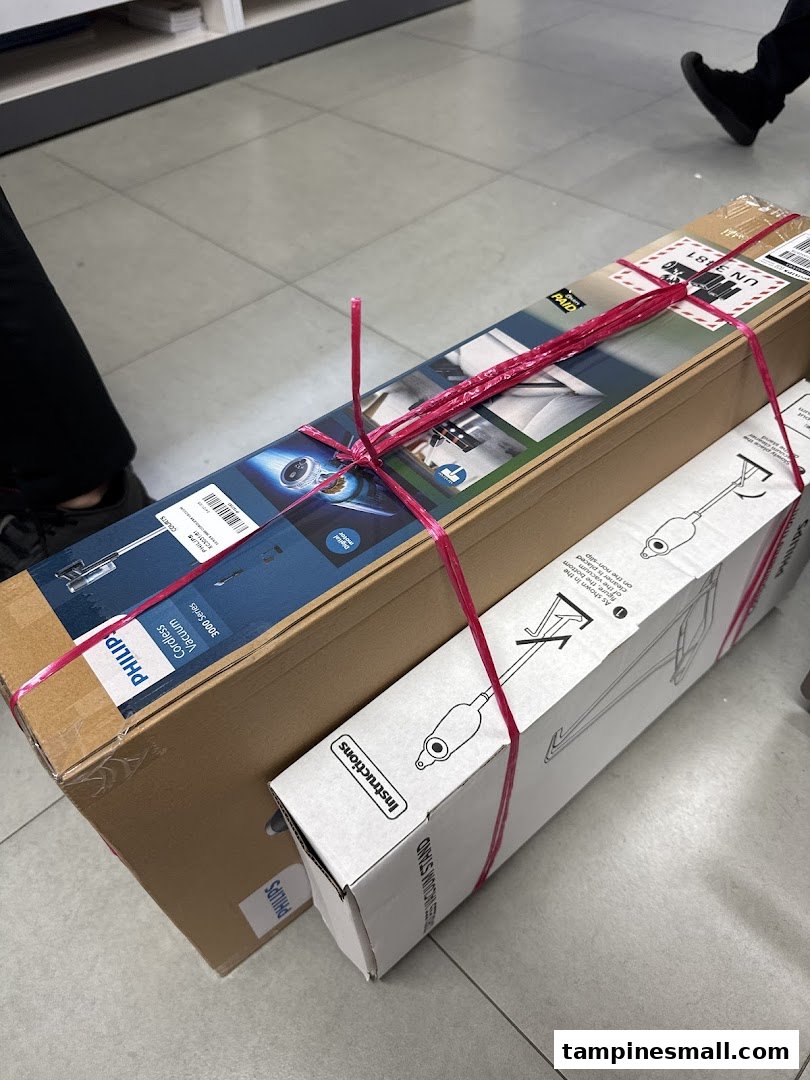 Two boxed Philips products, a cordless vacuum and a stand, tied together with pink string, on a tiled floor.