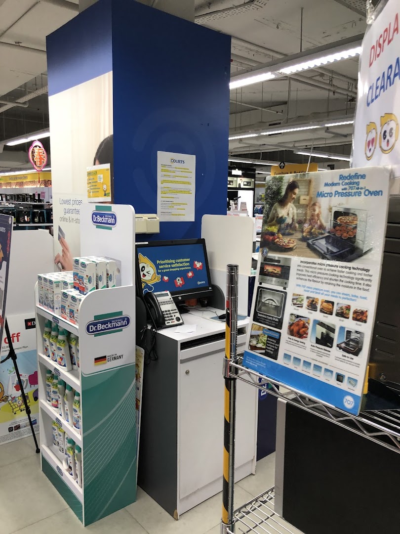 An in-store view of COURTS, featuring a customer service point, product displays, and promotional signage.