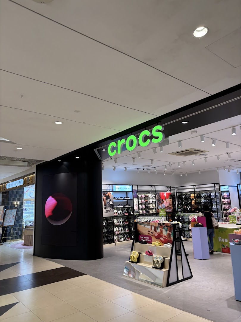 The bright green Crocs logo illuminates the entrance of a retail store in a shopping mall.