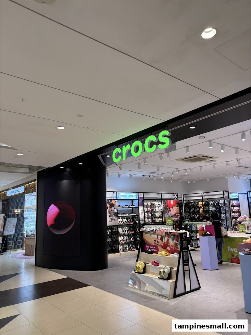 The bright green Crocs logo illuminates the entrance of a retail store in a shopping mall.
