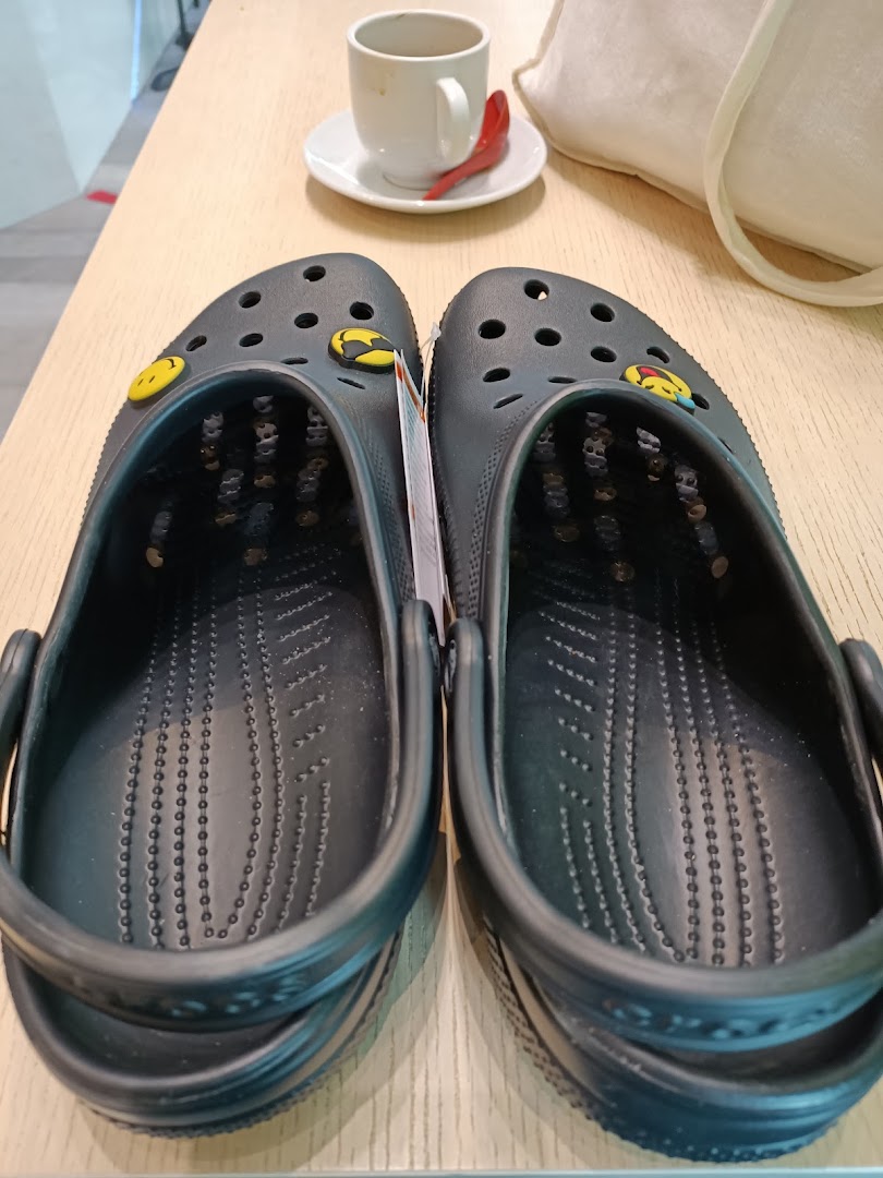 A pair of black Crocs clogs with yellow Jibbitz charms on a wooden table.