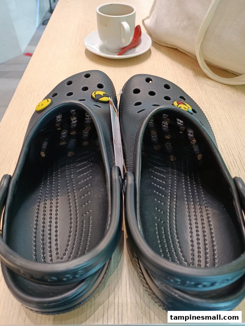 A pair of black Crocs clogs with yellow Jibbitz charms on a wooden table.
