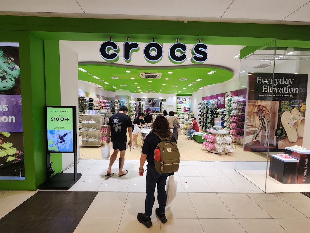 The vibrant green entrance of a Crocs store, showcasing a wide array of colorful footwear and a digital display.