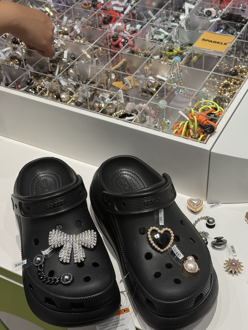 Two black Crocs clogs customized with decorative charms are displayed near a charm selection.
