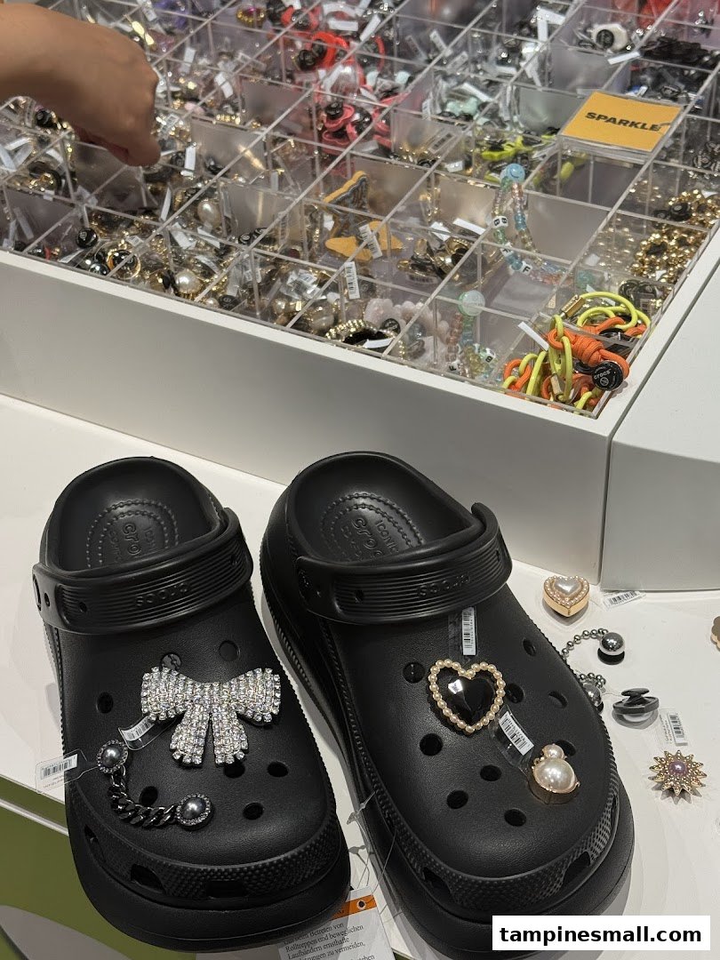 Two black Crocs clogs customized with decorative charms are displayed near a charm selection.