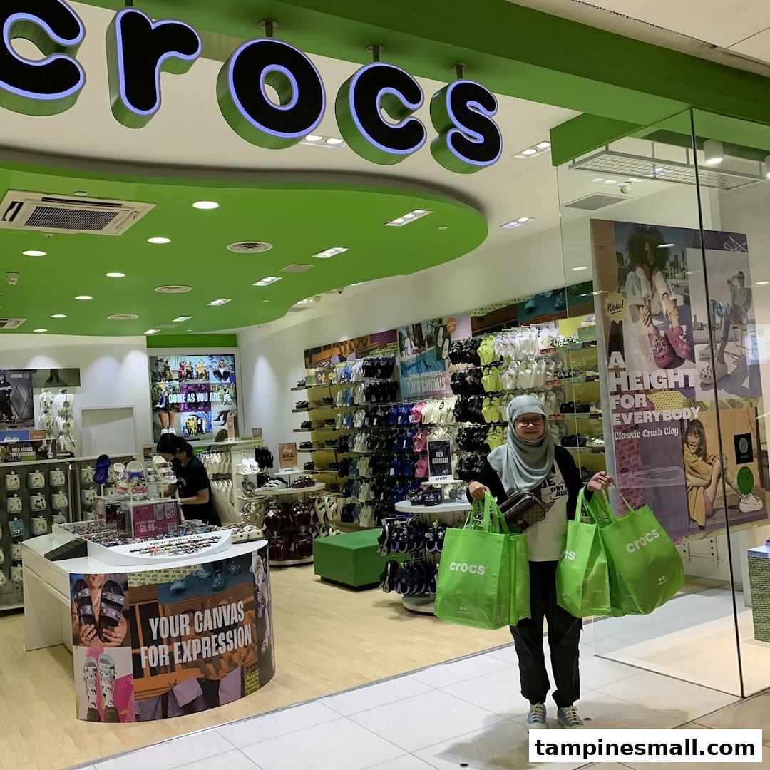 A customer stands outside the Crocs store entrance, holding several bright green shopping bags.