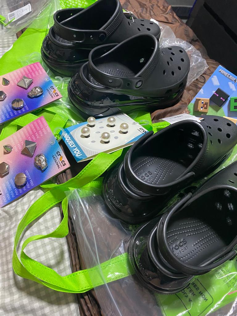 Black Crocs clogs and various Jibbitz charms, including pearl and metallic designs, on a green bag.