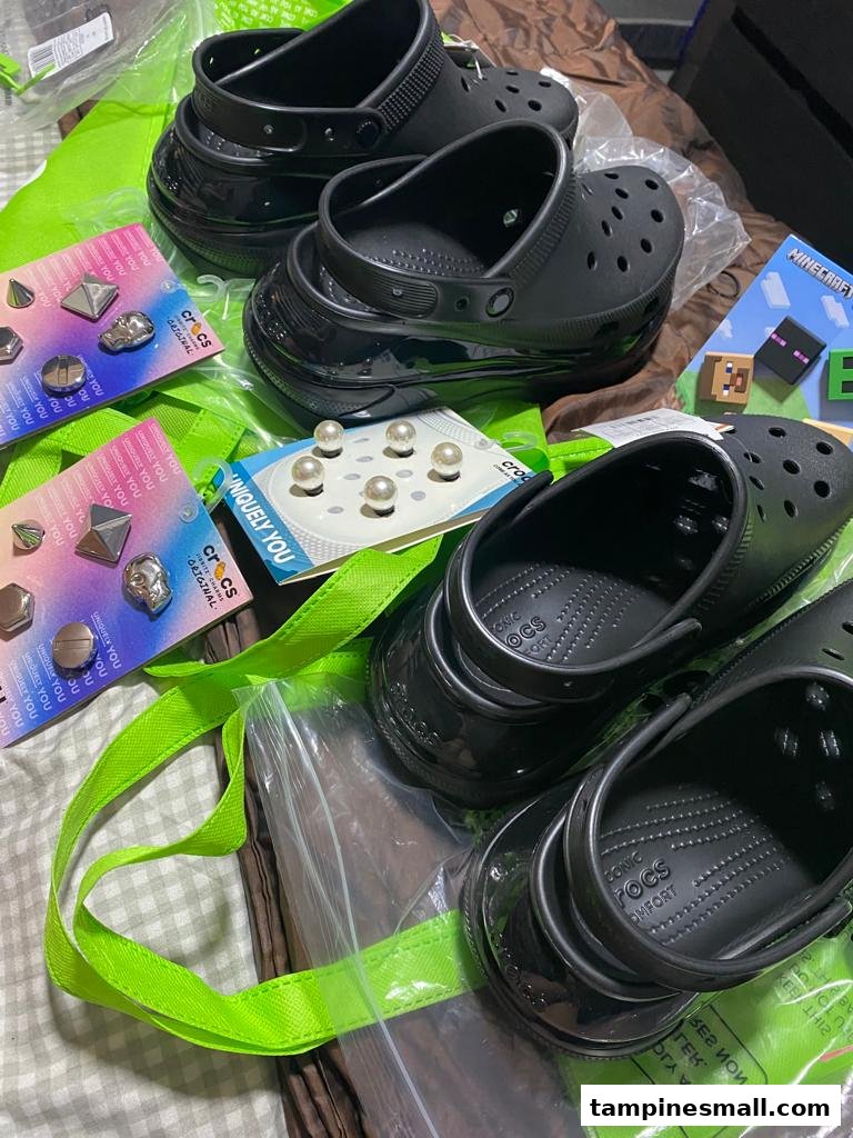 Black Crocs clogs and various Jibbitz charms, including pearl and metallic designs, on a green bag.