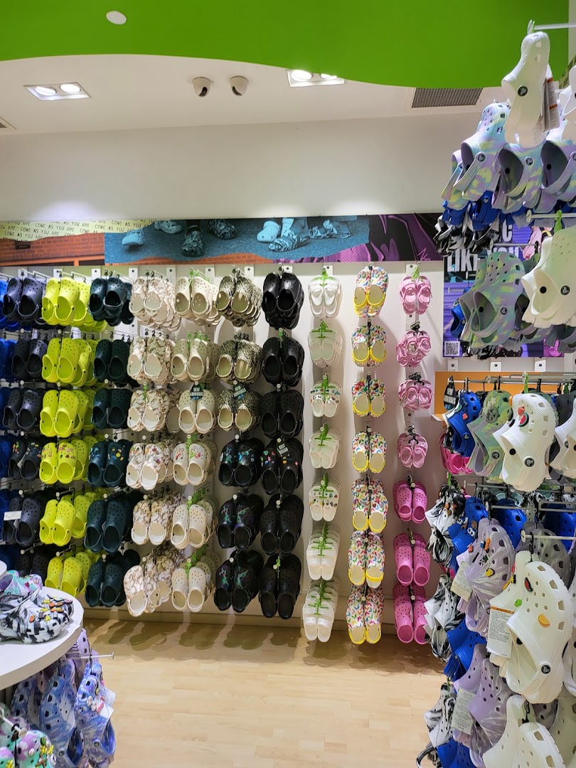 A vibrant wall display showcasing a wide variety of colorful Crocs clogs and sandals in a retail store.