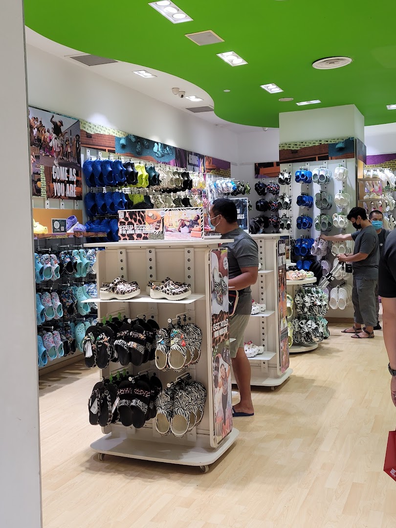 Customers browse colorful Crocs footwear and accessories inside a brightly lit Crocs store.