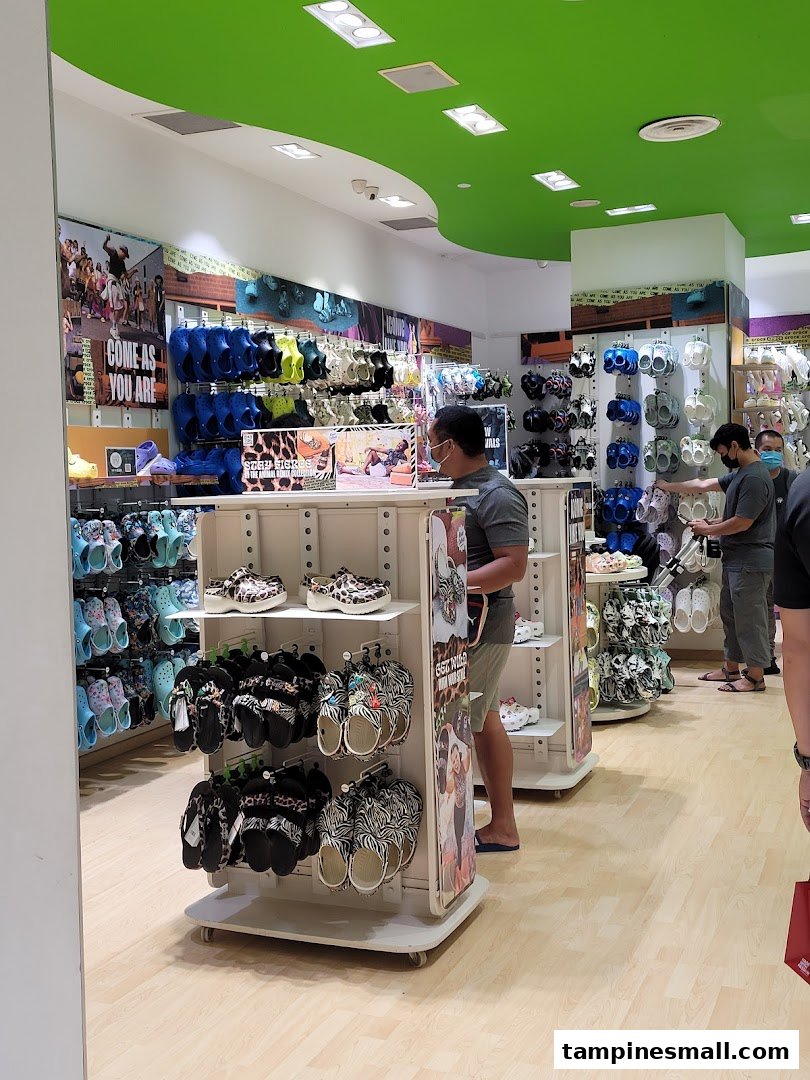 Customers browse colorful Crocs footwear and accessories inside a brightly lit Crocs store.