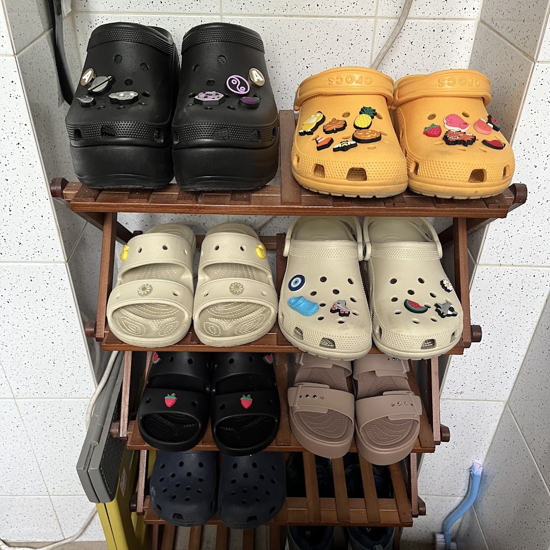 A display of various Crocs footwear, including clogs and sandals, on a wooden shoe rack.