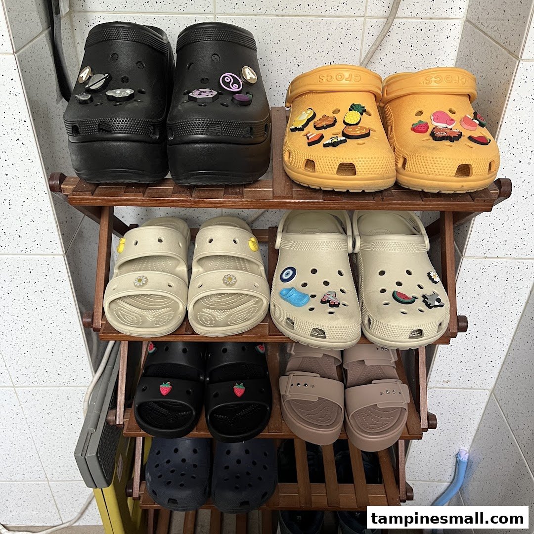 A display of various Crocs footwear, including clogs and sandals, on a wooden shoe rack.