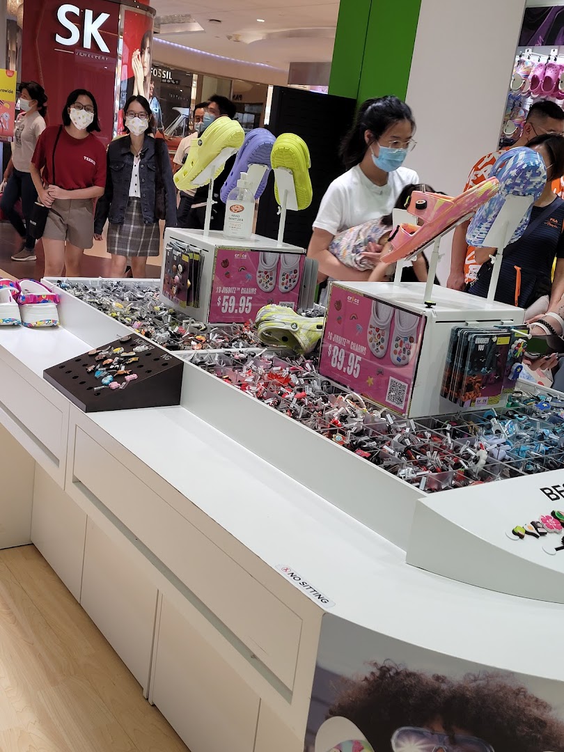 A vibrant display of Crocs Jibbitz charms and footwear inside a bustling mall environment.
