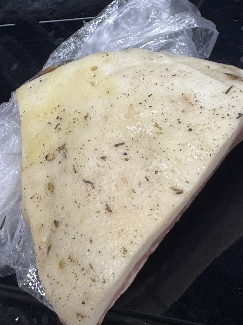 A close-up of a seasoned piece of pork belly, partially wrapped in plastic, from Cut Butchery.