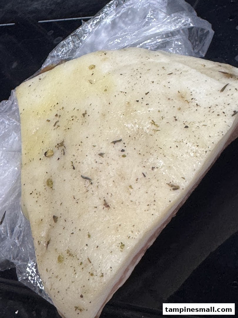 A close-up of a seasoned piece of pork belly, partially wrapped in plastic, from Cut Butchery.