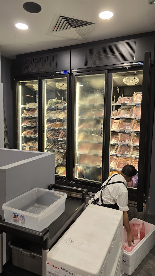 A staff member restocking packaged meat products in large display refrigerators at Cut Butchery.