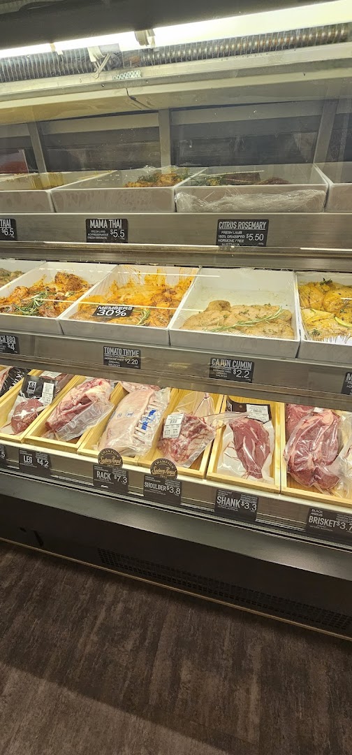 A refrigerated display case showcasing various fresh and marinated meat cuts at a butchery.