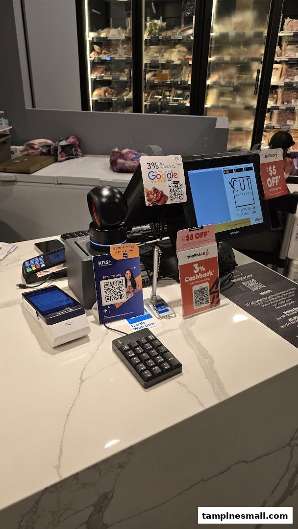 A well-lit checkout counter at Cut Butchery, featuring payment terminals and refrigerated meat displays in the background.