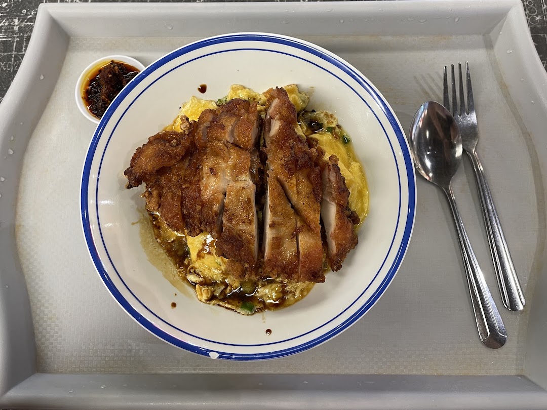 A delicious plate of scrambled egg rice topped with crispy fried chicken, served with sauce and cutlery.