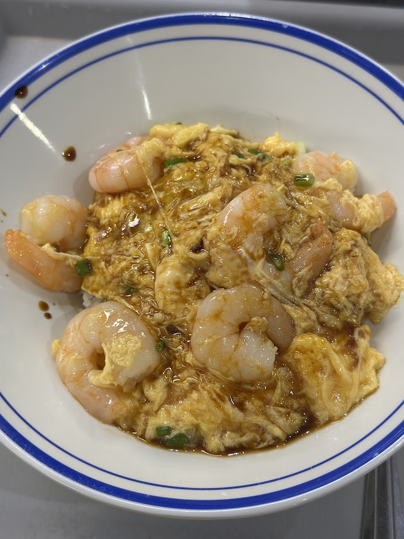 A close-up of a bowl of scrambled egg rice topped with succulent shrimp and savory sauce.