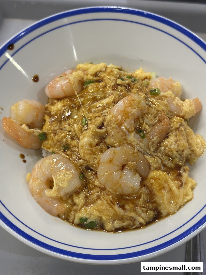 A close-up of a bowl of scrambled egg rice topped with succulent shrimp and savory sauce.