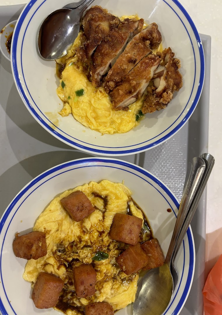 Two bowls of fluffy scrambled egg rice, one with crispy fried chicken, the other with savory luncheon meat.