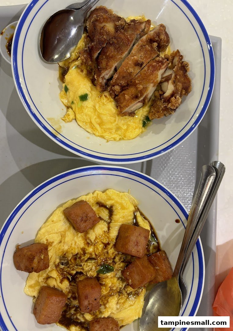 Two bowls of fluffy scrambled egg rice, one with crispy fried chicken, the other with savory luncheon meat.