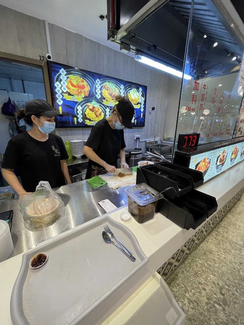 Two staff members preparing food at a counter with a digital menu board displaying scrambled egg rice dishes.