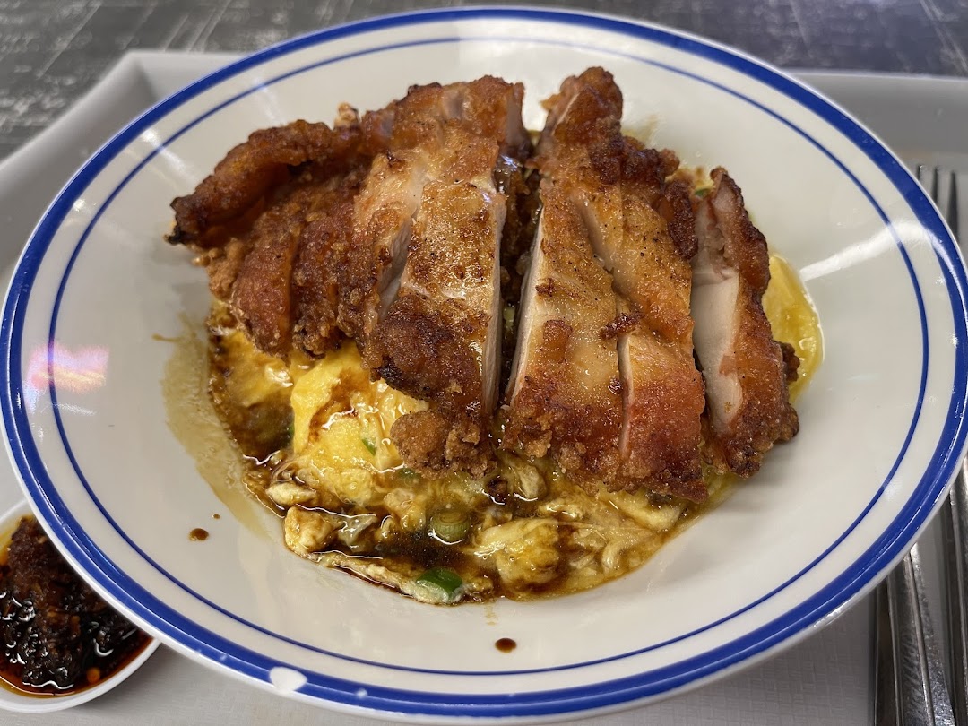 A delicious plate of crispy fried chicken served over fluffy scrambled egg rice with a side of chili oil.