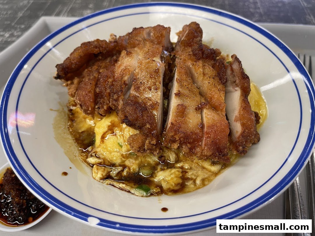 A delicious plate of crispy fried chicken served over fluffy scrambled egg rice with a side of chili oil.