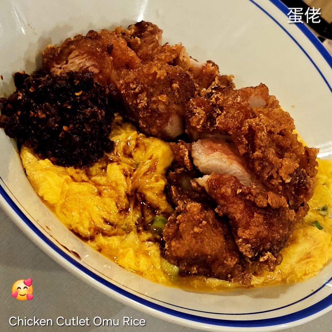 A close-up of a delicious chicken cutlet omu rice bowl with fluffy scrambled egg and chili.