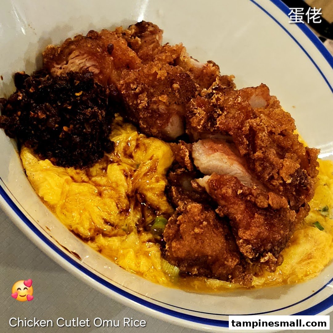 A close-up of a delicious chicken cutlet omu rice bowl with fluffy scrambled egg and chili.