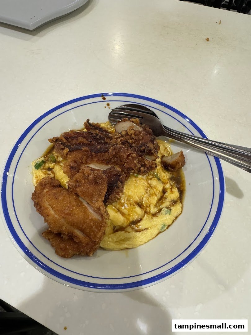 A close-up of a bowl of scrambled egg rice topped with crispy fried chicken and a spoon.