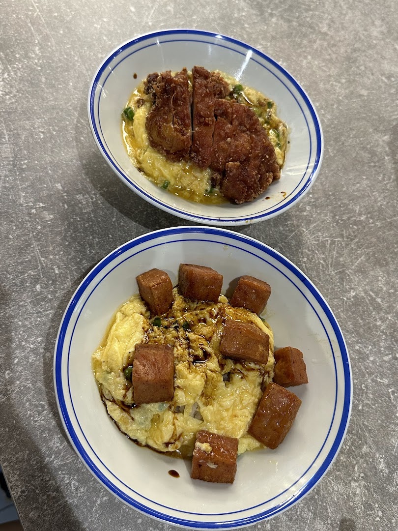 Two bowls of scrambled egg rice, one with fried chicken cutlet and one with spam.