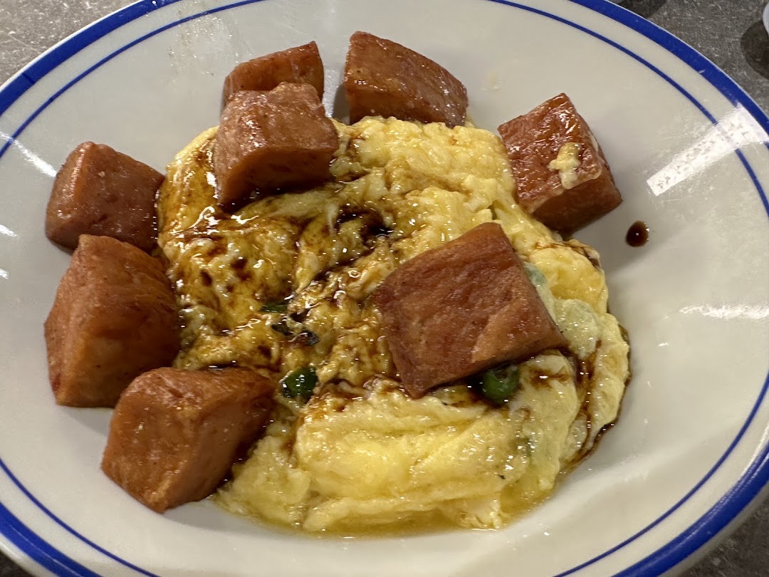 A close-up of fluffy scrambled eggs topped with generous cubes of luncheon meat and a savory sauce.