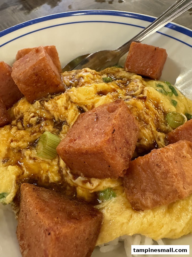 A close-up of scrambled egg rice topped with crispy fried spam cubes and a savory sauce.