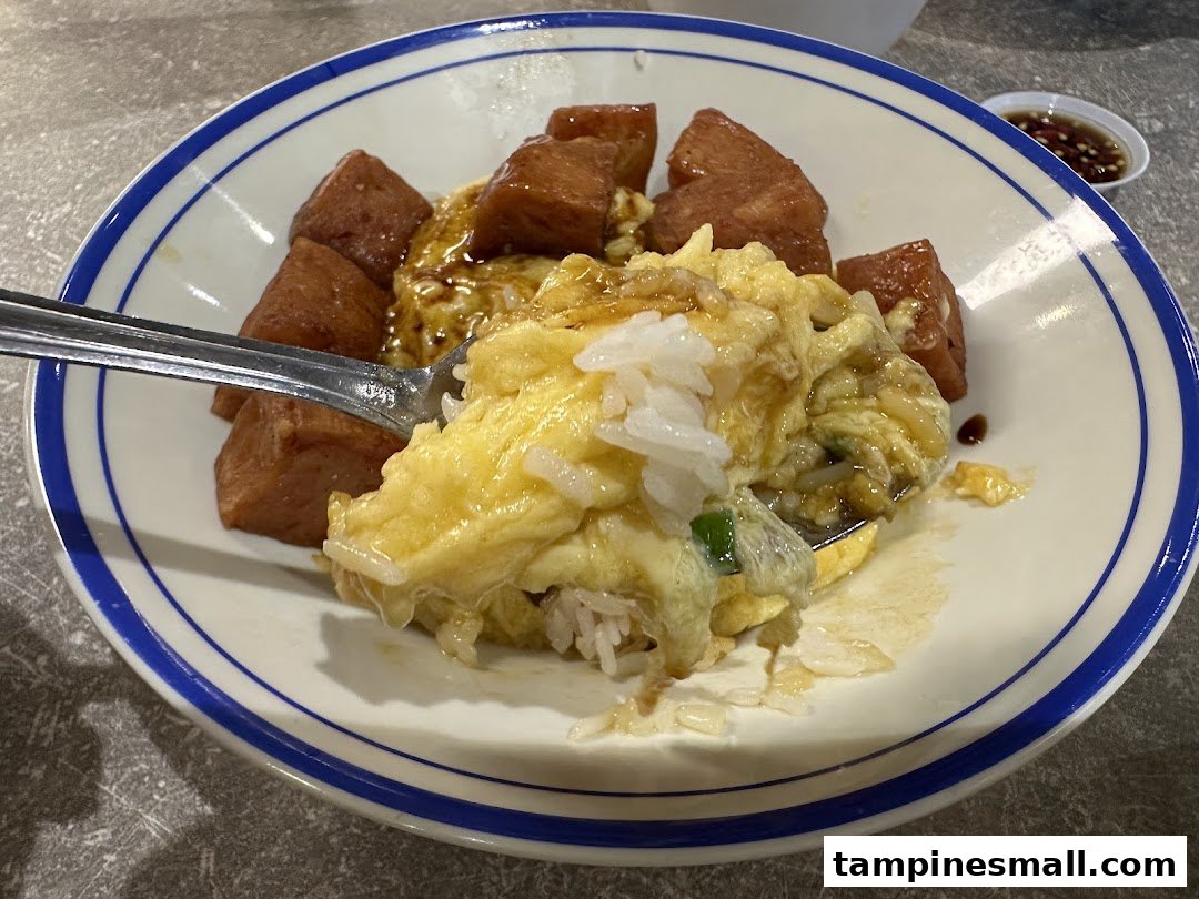 A close-up of scrambled egg rice with spam, served in a classic blue-rimmed bowl.